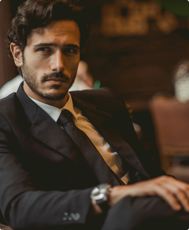 Man in suit sitting indoors with serious expression.