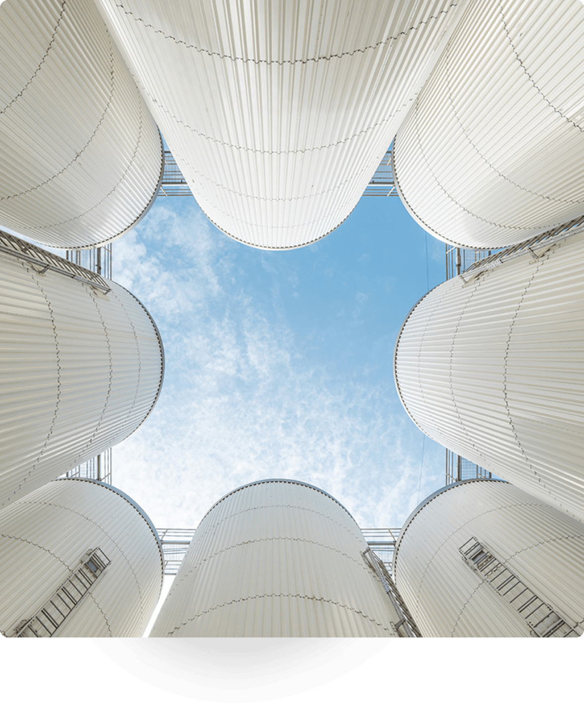 Looking up at tall industrial silos with blue sky above.
