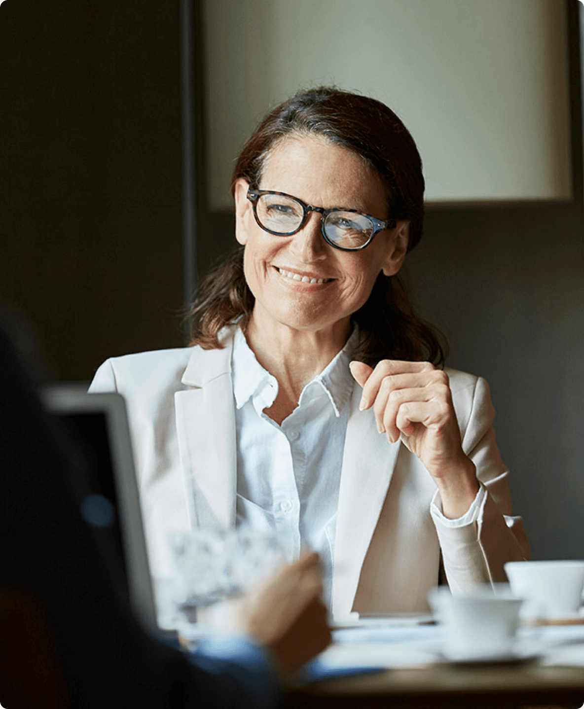 Professional woman in glasses and blazer smiling during a meeting.