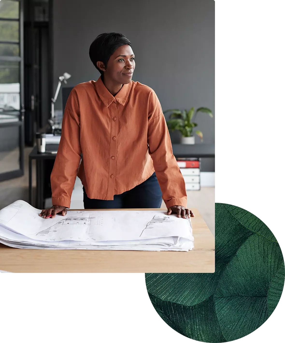 Architect in orange shirt leaning over desk with blueprint sheets.