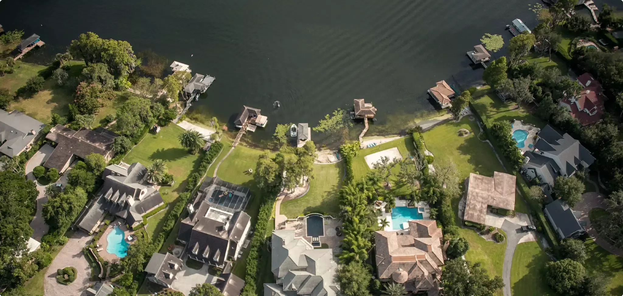 Aerial view of waterfront homes with docks, pools, and green yards.
