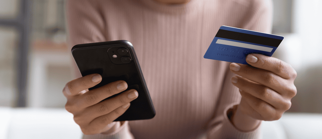 A smiling woman is looking at her phone and checking her business debit account after preventing an AI scam.