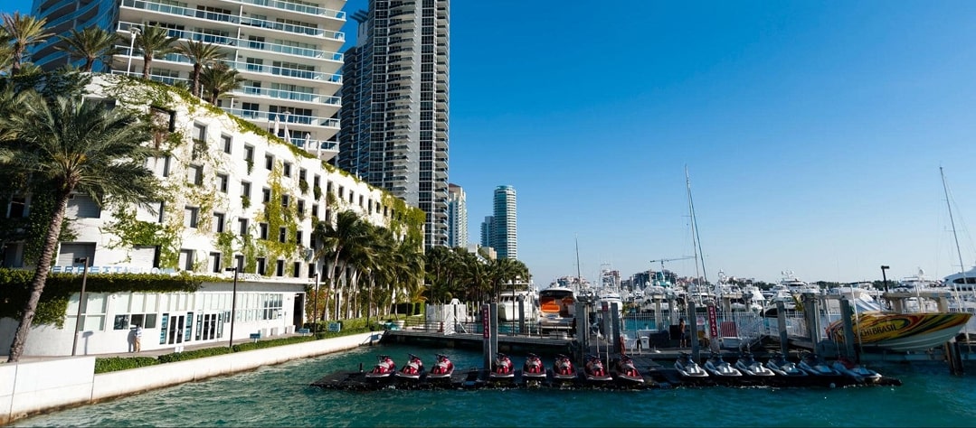 Luxury high-rise buildings and a marina with jet skis on a sunny day in Miami, Florida.