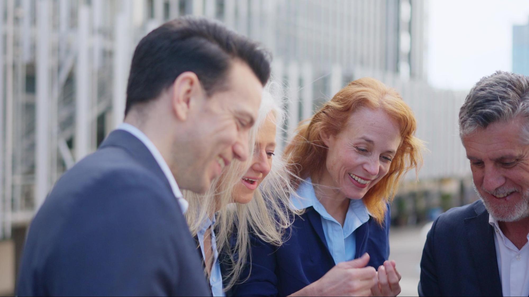 A group of business professionals is smiling while reviewing plans on a tablet outdoors, symbolizing collaboration in commercial real estate loans.