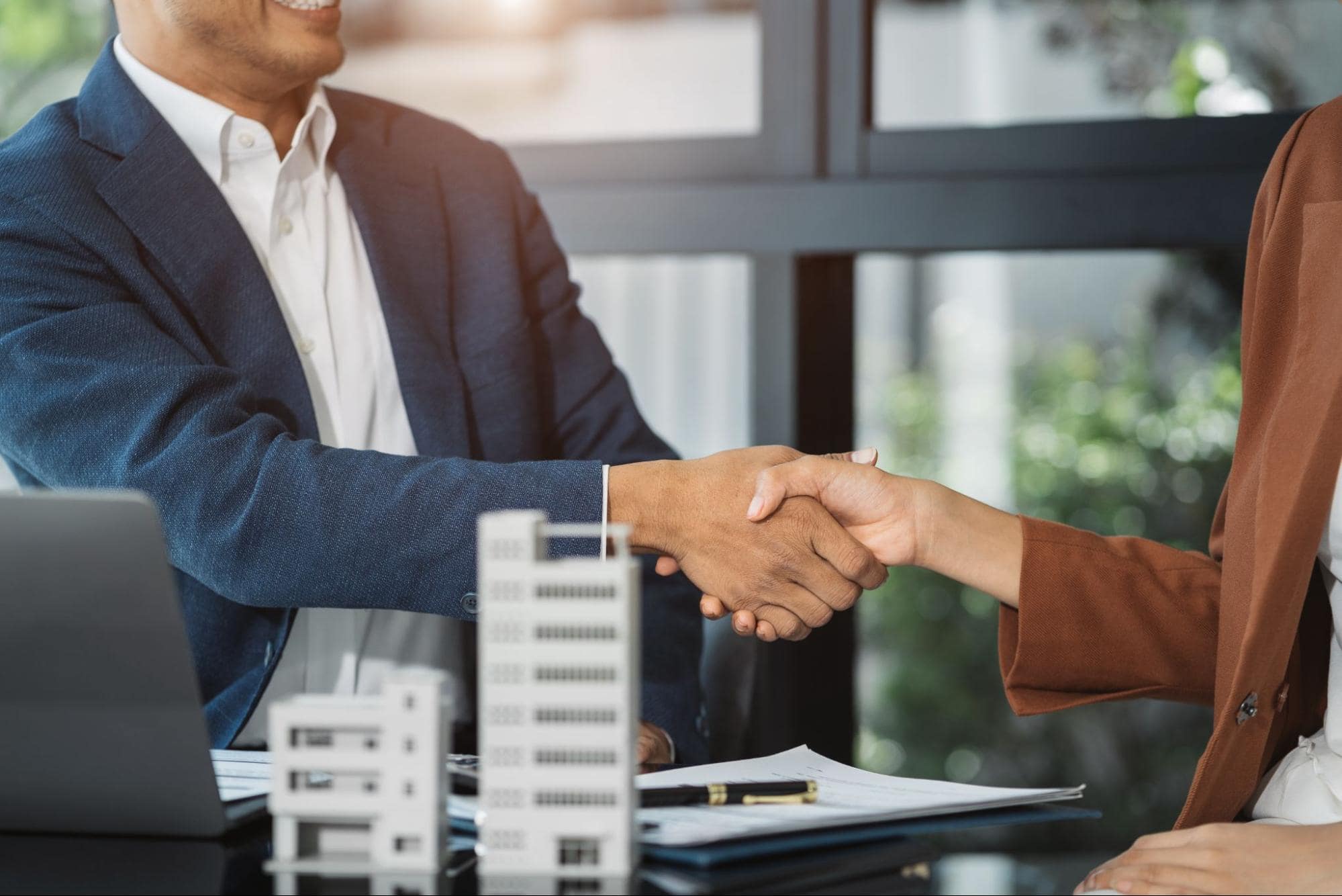 Close-up of a professional handshake over loan documents and building models, representing a commercial real estate loan agreement.