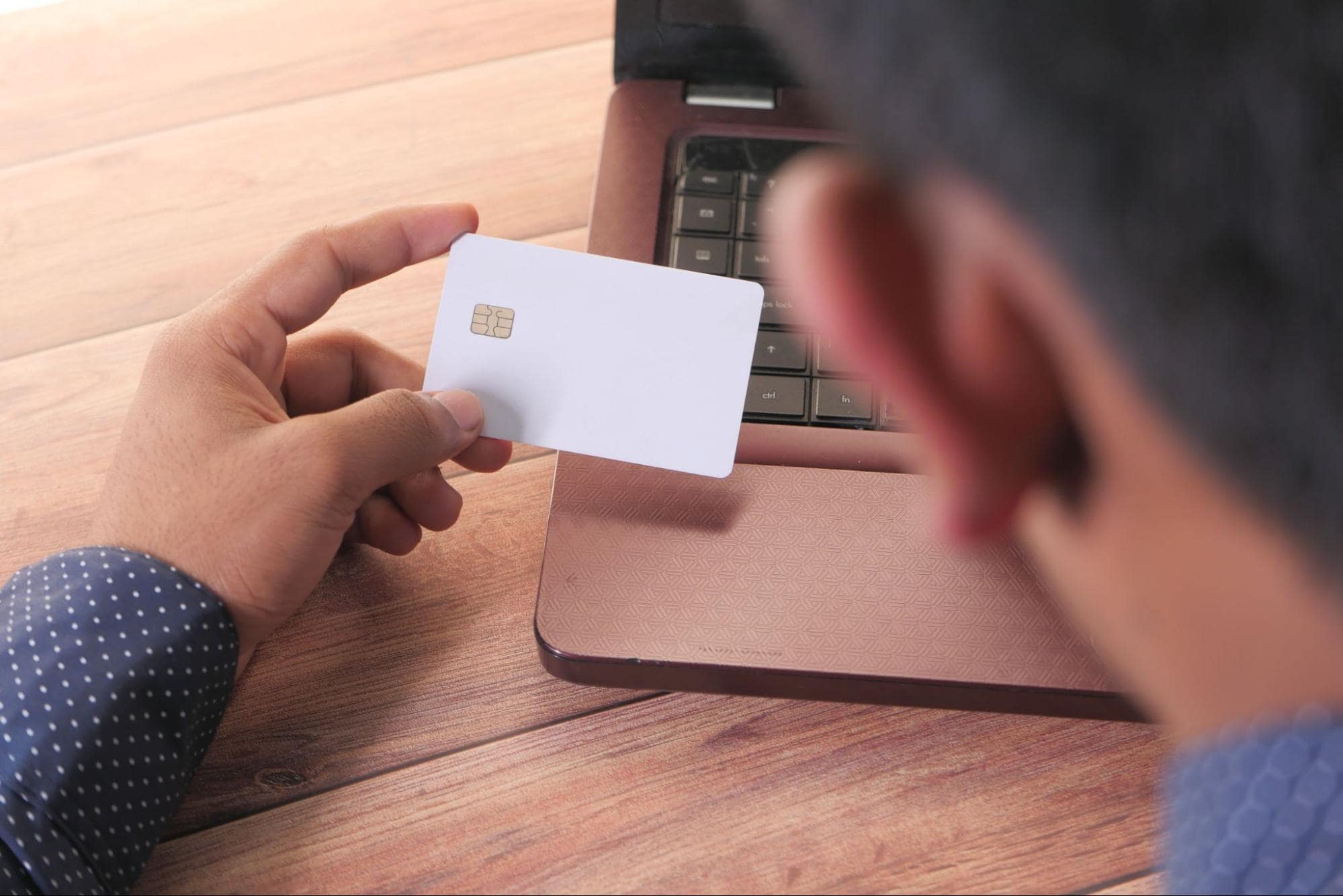Man holding a credit card in front of his laptop, highlighting common signs of financial scams linked to online fraud and phishing attempts.